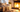 Cozy holiday scene with a chunky knit throw draped over a cream sofa beside a glowing fireplace, soft candlelight and warm bokeh lights creating a relaxing Christmas atmosphere.